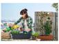 Een vrouw plant bloemen in een zwarte bloempot op een balkon.