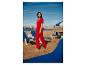Femme en combinaison rouge marchant pieds nus sur une plage de sable avec des transats.