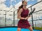 Femme en robe de padel marron avec raquette sur un court de padel extérieur.