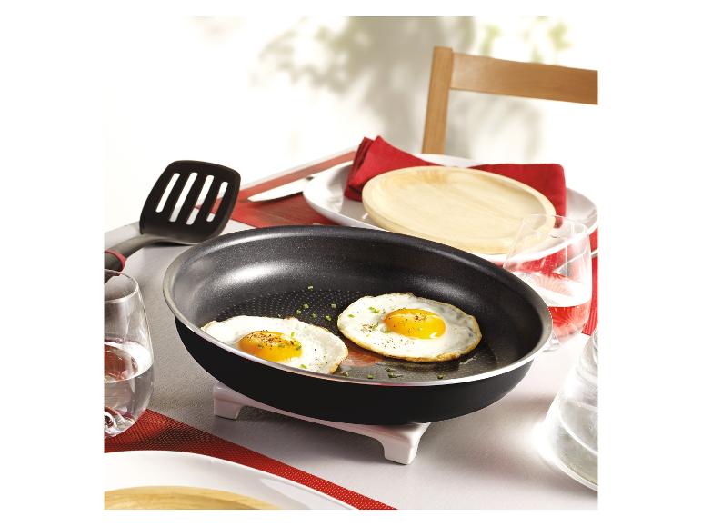 Deux œufs au plat dans une poêle noire sur une table avec des sets de table rouges.