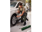 Een man in groene overall en beige T-shirt draait een wielmoer vast aan een witte auto.