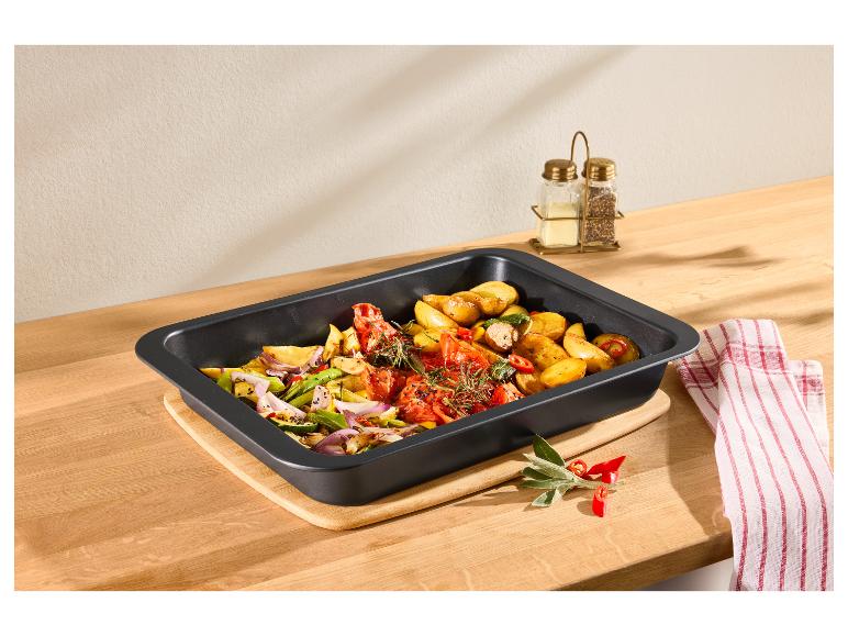 Ovenschaal met geroosterde groenten, aardappelen, tomaten en uien op een houten plank.