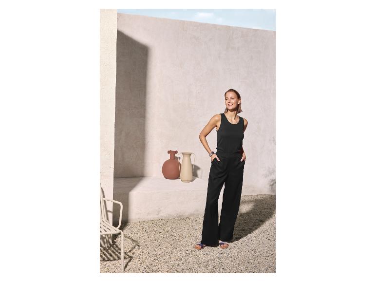 Femme en débardeur noir et pantalon large noir dans une cour ensoleillée.