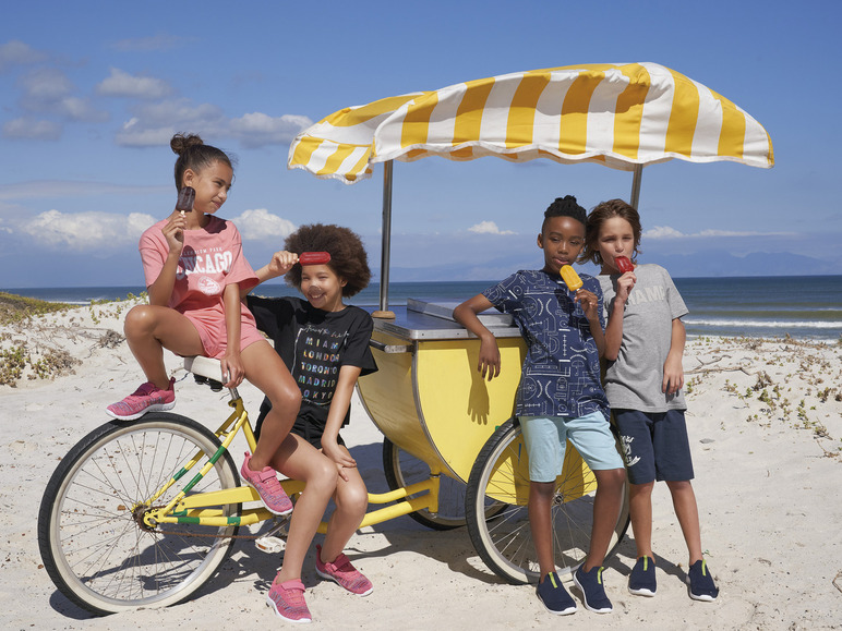 Des enfants sur la plage avec des glaces, un vélo et un chariot de plage.