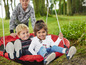 Twee kinderen zitten in een rode schommel in de tuin.