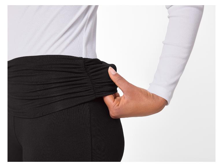 Vrouw in wit shirt met lange mouwen en zwarte leggings met geplooide taille.