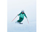 Een vrouw skiënd in een groene skipak, helm en ski-bril.