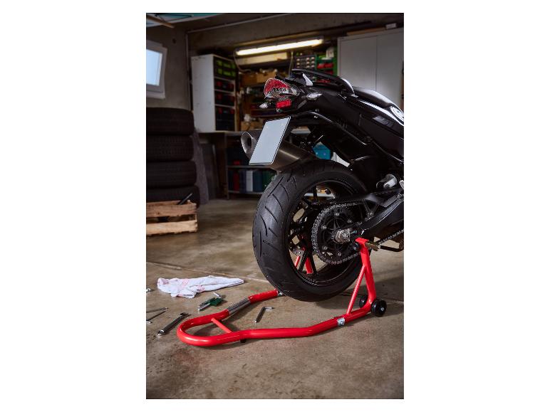 Rode achterbok voor motorfiets in een garage met gereedschap op de vloer.