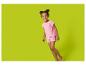 Fille souriante en pyjama rose à pois, debout sur un fond vert.