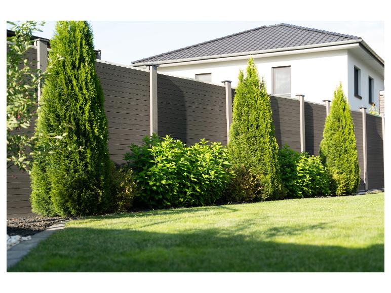 Moderne tuinafscheiding van donkere planken, groene struiken en gazon.