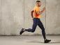 Man in een oranje T-shirt en blauwe leggings hardlopend voor een betonnen muur.