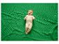Blije baby in beige slaappak op een groene wafel deken