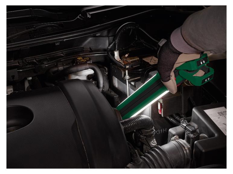 Een monteur gebruikt een lamp om de motor van een auto te inspecteren.