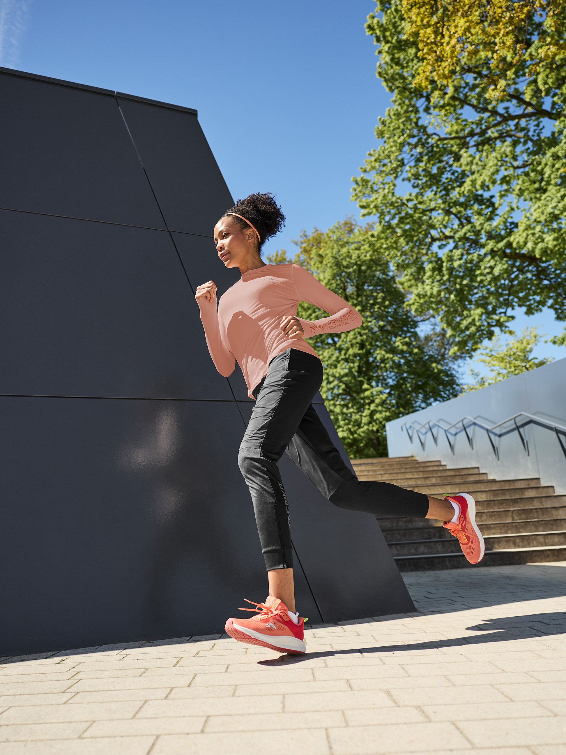 Vrouw in hardloopshirt met lange mouwen en broek, buiten aan het hardlopen.