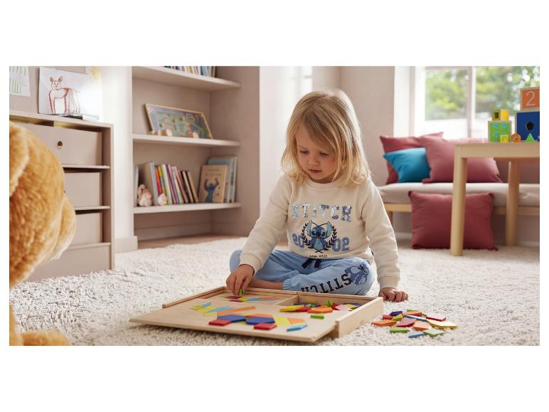 Enfant jouant avec un puzzle en bois de formes géométriques sur un tapis.