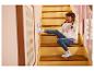 Fille joyeuse en jean et sweat arc-en-ciel assise sur les escaliers, montrant des baskets.