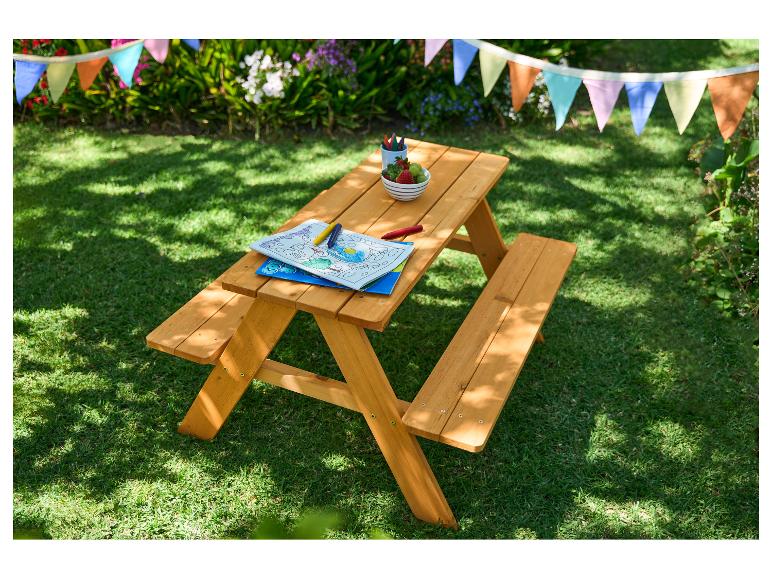Table de pique-nique en bois pour enfants avec livre de coloriage, crayons et fruits dans un jardin.
