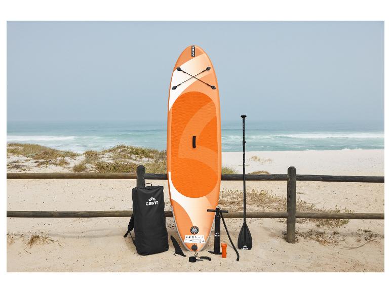 Planche de SUP orange et blanche avec accessoires sur une plage de sable près de la mer.
