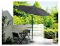 Een grijze parasol met een stenen voet, een zwarte tafel en stoelen op een patio