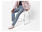 Personne en trench-coat rose, jean bleu et baskets beiges assise sur un tabouret en métal.