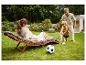 Vrouw ontspant op een tuinstoel terwijl een man en kind voetballen.