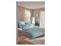 Slaapkamer met bed met mintgroen beddengoed, beige gordijnen en houten vloer.