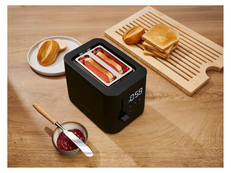 Zwarte broodrooster met brood dat roostert, toast, broodjes en jam op een houten tafel.