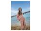 Lachende vrouw in roze pyjama op een zonnig strand.