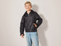 Een jongen draagt ​​een zwarte leren jas en blauwe jeans.