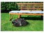 Tondeuse robot sur pelouse verte devant un banc en bois avec des coussins.