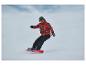Snowboarder en veste rouge à motifs et pantalon noir, sur un snowboard rouge.
