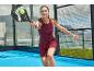 Vrouw speelt padel met racket en bal op een blauw veld.