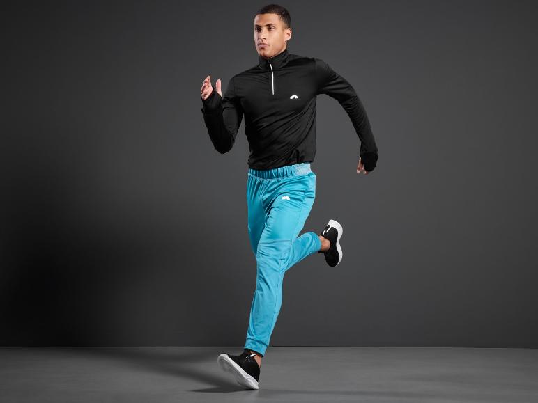 Un homme court en pantalon de survêtement noir et bleu.