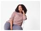 Femme en t-shirt rose et leggings gris, assise sur une chaise transparente.