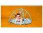 Lachende baby op een speelmat met hangend speelgoed, oranje achtergrond.