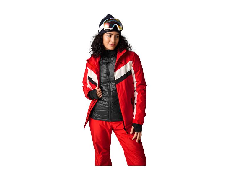Vrouw in rode en zwarte ski-jas en skibroek met skibril en muts.