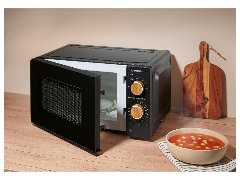 Zwarte magnetron met open deur, naast een kom tomatensoep en een houten snijplank.