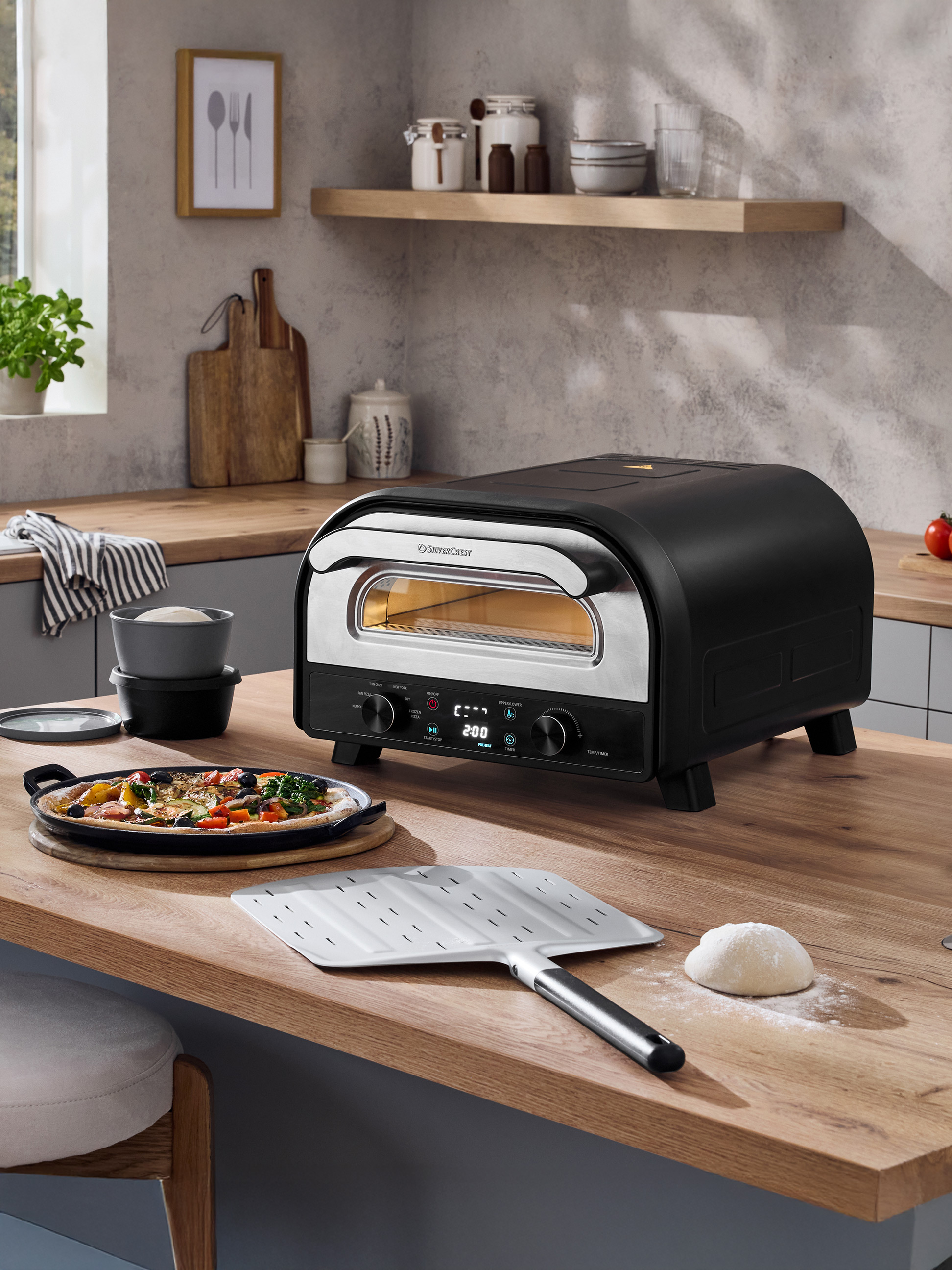 Zwarte pizzaoven op een houten aanrecht met een vers bereide pizza en deeg.