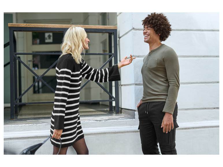 Une femme avec une robe à rayures noires et blanches et un homme avec un pull vert et un pantalon noir.