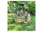 Enfants jouant à une table de jardinage en bois avec tableau, avec cabane dans les arbres et bac à sable en arrière-plan.