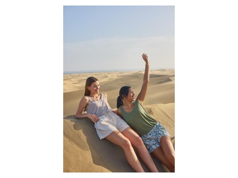 Deux femmes en débardeurs et shorts se détendent sur des dunes de sable.