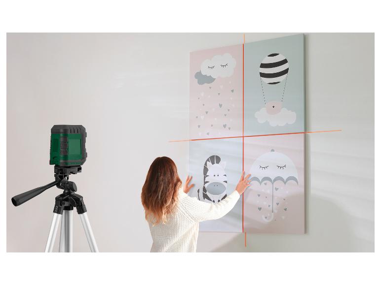 Vrouw gebruikt laserwaterpas om kinderfoto's aan de muur te hangen.