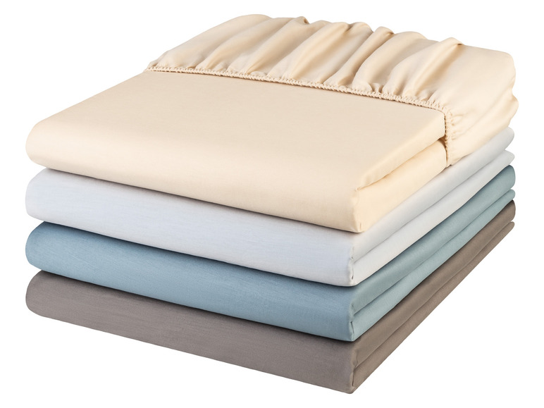Une pile de quatre draps en beige, blanc, bleu et gris.