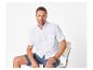 Homme en chemise blanche à manches courtes et short bleu marine, assis sur une chaise.