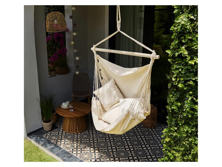 Chaise suspendue en tissu avec coussins sur un patio avec carrelage et plantes.
