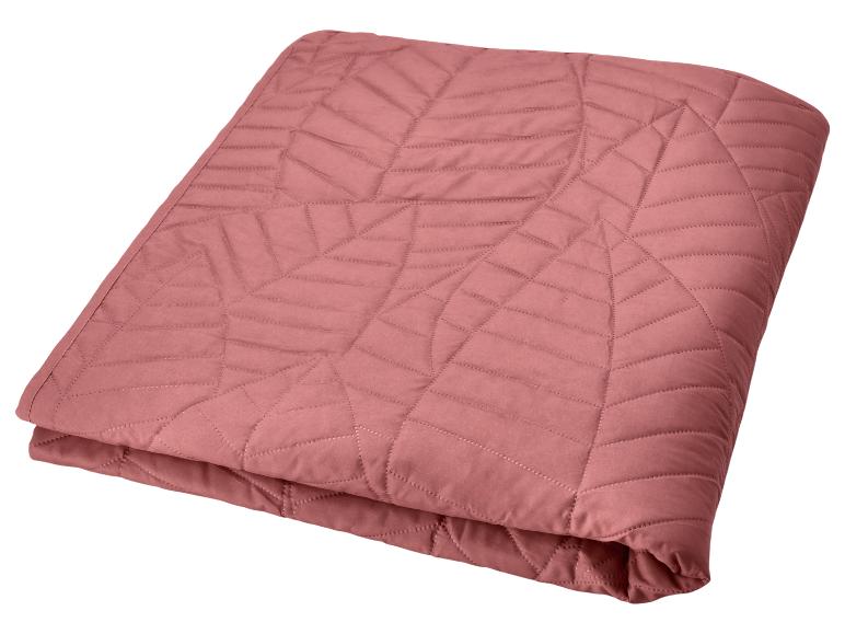Jeté de lit matelassé rose avec motif géométrique.