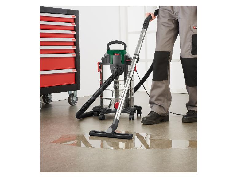 Een man reinigt een plas water met een nat-/droogzuiger naast een gereedschapskast.