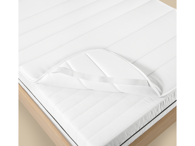 Witte matrasbeschermer en matras op een houten bedframe.