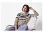 Lachende vrouw in een beige gebreide trui, jeans en gouden oorbellen, zittend op een stoel.