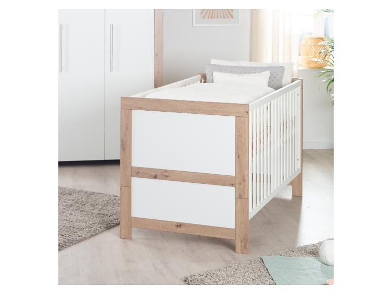 Wit en houten ledikant met beddengoed in een lichte kinderkamer.